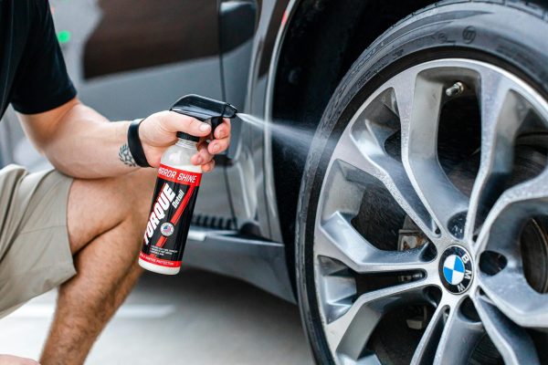 Person using a spray bottle to clean the rim of a car wheel outdoors.